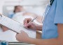image of nurse writing on clipboard with patient in bed
